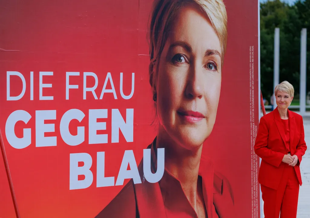 Manuela Schwesig in a red pantsuit next to a red election poster with a picture of her face, with the text