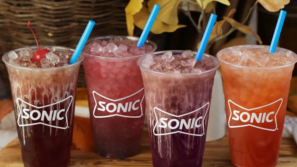 Four Sonic beverages in clear cups with ice and blue straws, one with a cherry.