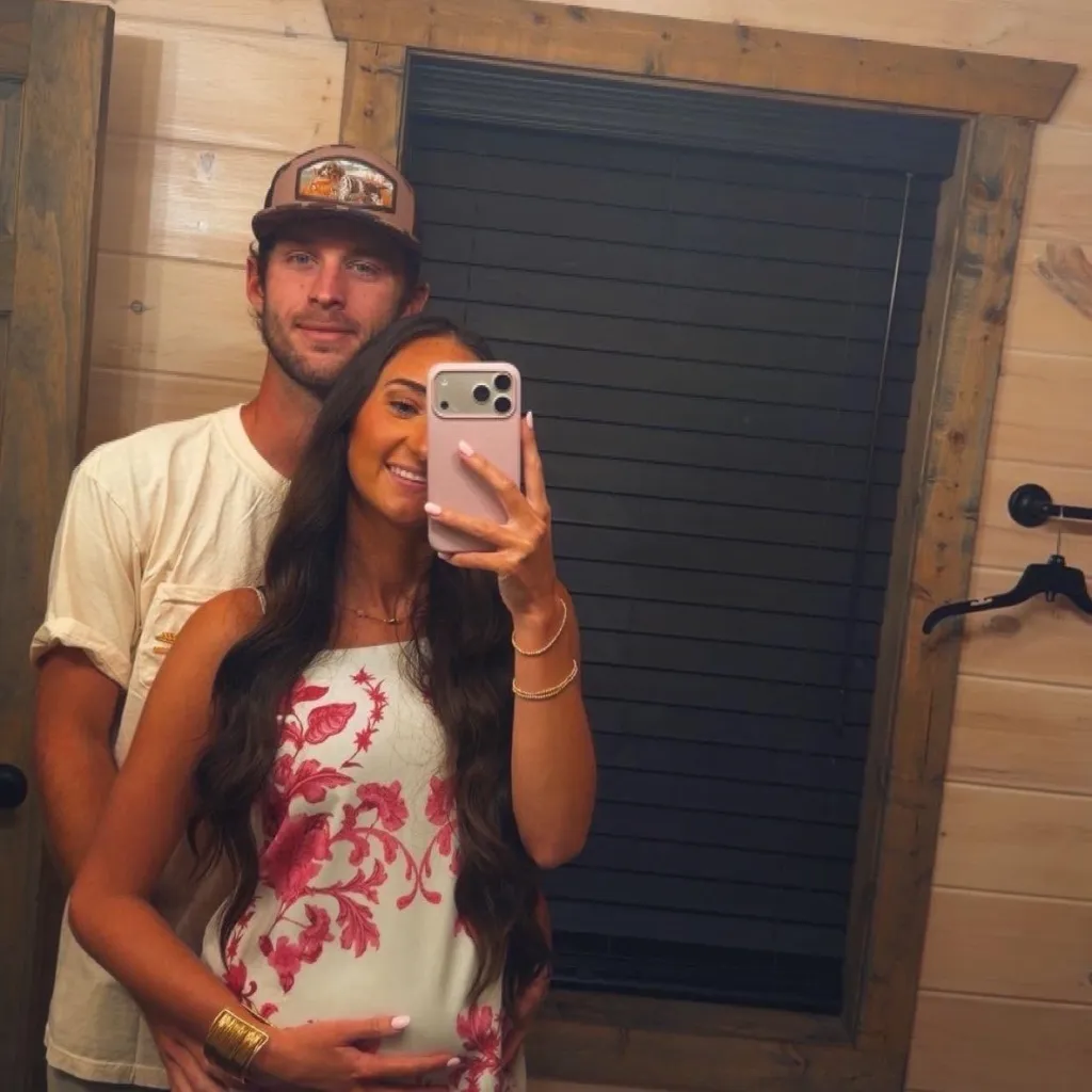Baylee Johnson taking a mirror selfie with her partner, showing her baby bump.