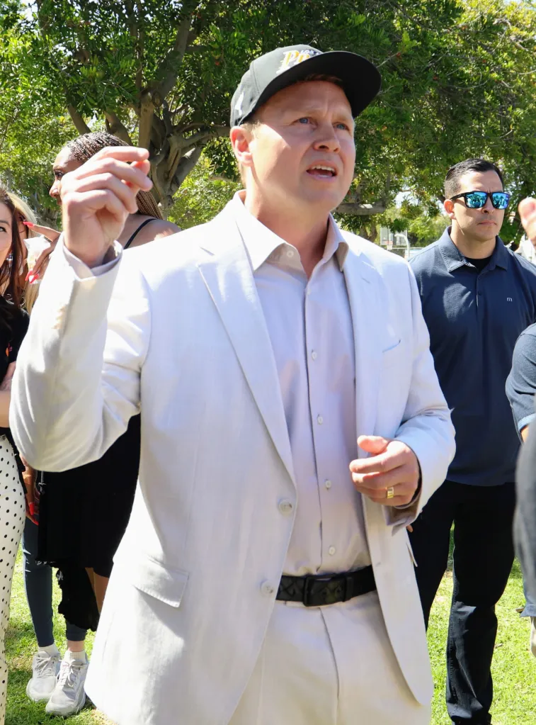 Spencer Pratt in a light suit and baseball cap speaking outdoors.