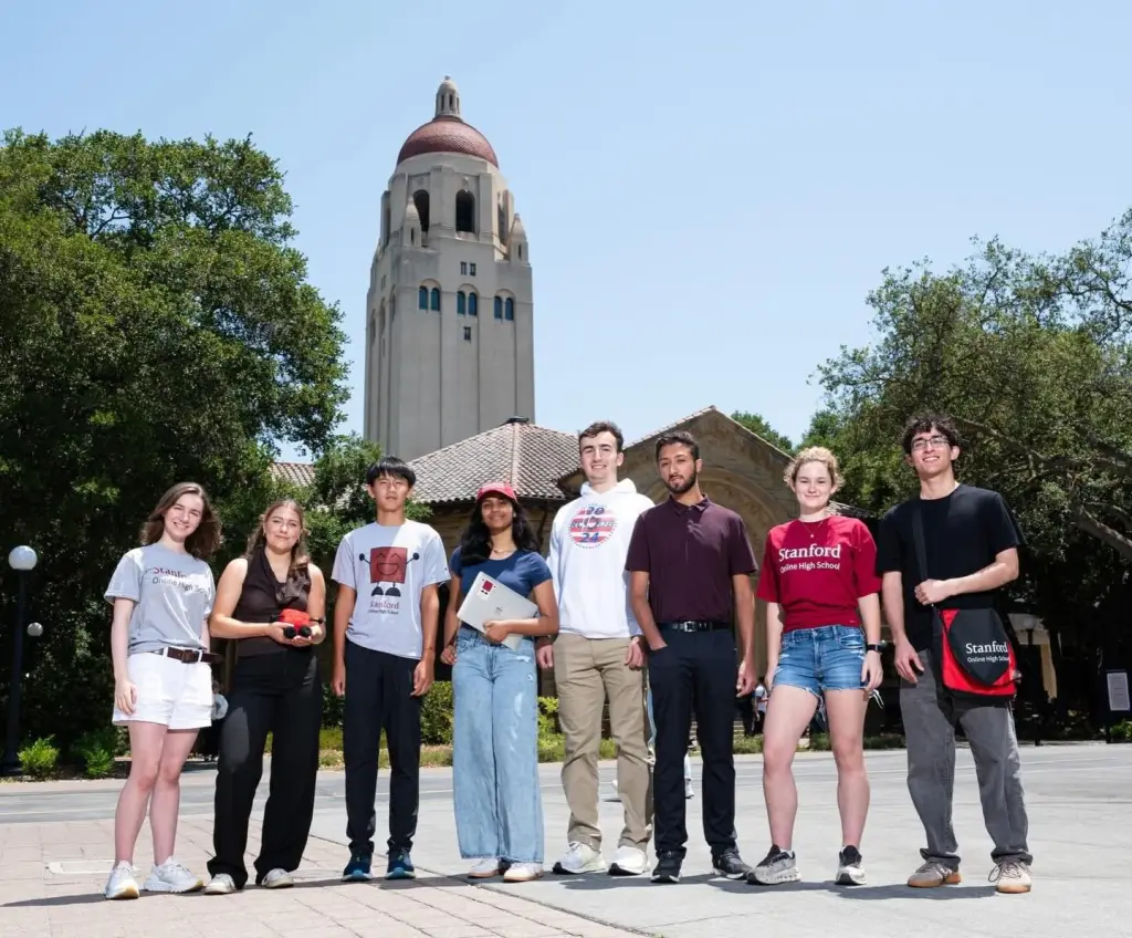 Seven Stanford Online High School students stand in front of a campus building with a domed tower.