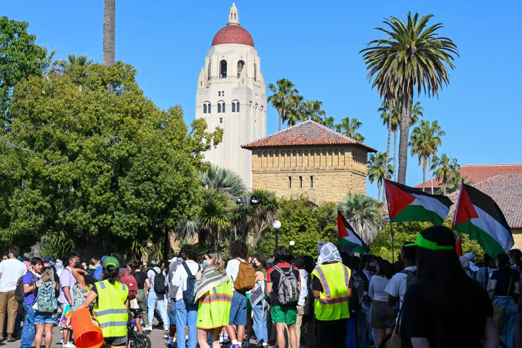 Students protest Israeli attacks on Gaza at Stanford University, with Palestinian flags and the Hoover Tower visible.