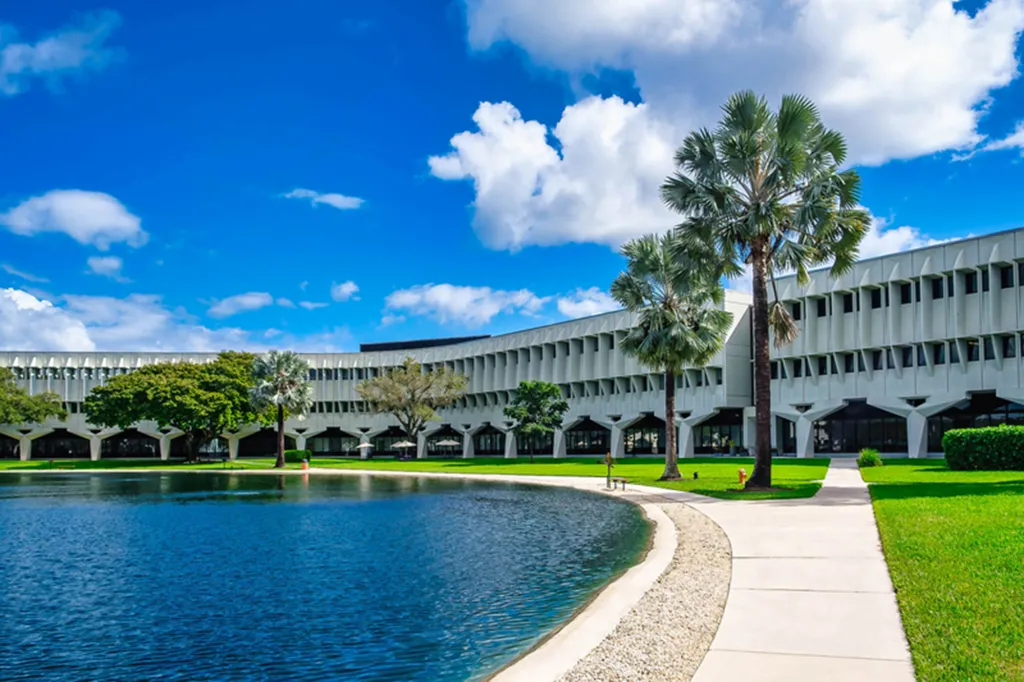 Building with a curved facade, a body of water in front, and palm trees.