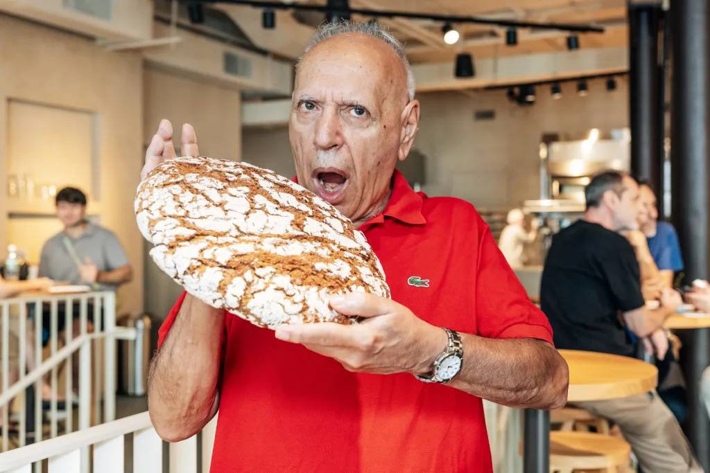 Steve Cuozzo at RYE by Martin Auer in Nolita holding a loaf of bread, mouth open in surprise.