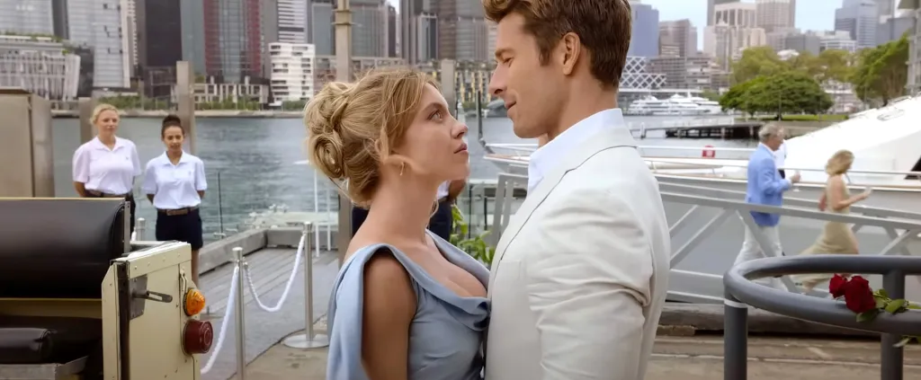Sydney Sweeney, in a blue gown, and Glen Powell, in a white suit and white shirt, gaze at each other in 