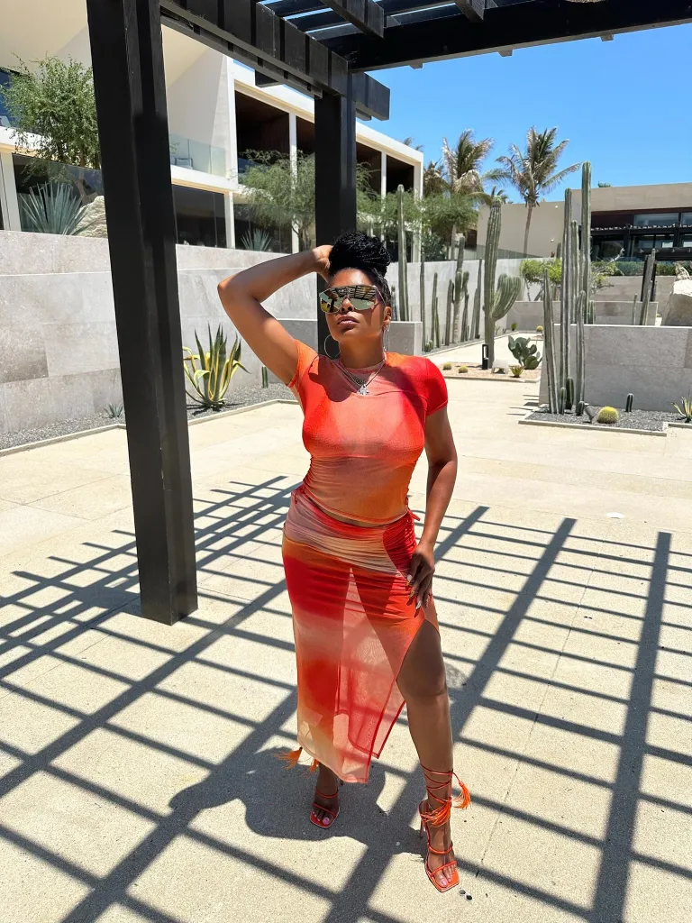 Taraji P. Henson posing outdoors in an orange dress and sunglasses.
