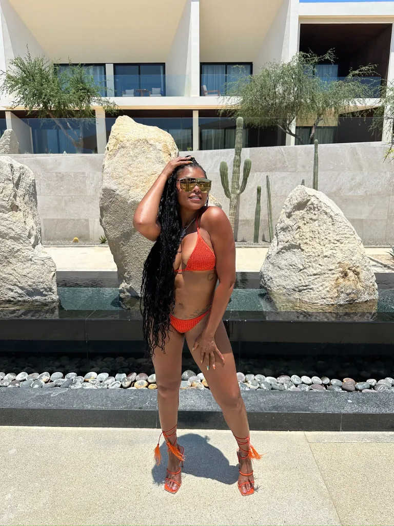 Taraji P. Henson in an orange bikini and heels posing outdoors.