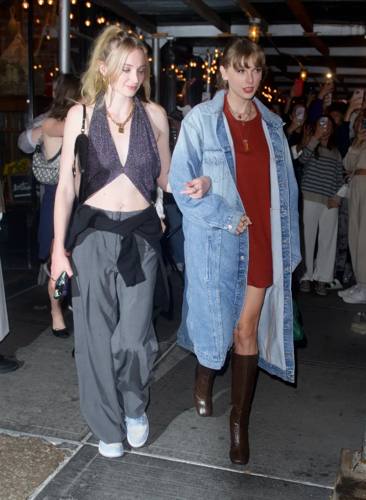 Taylor Swift in a long denim coat and a friend walking arm-in-arm.