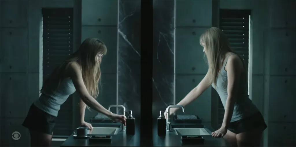 Taylor Swift looking at her reflection in a dark, modern bathroom.