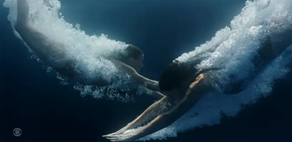 Two people diving into water, captured underwater as bubbles surround them.