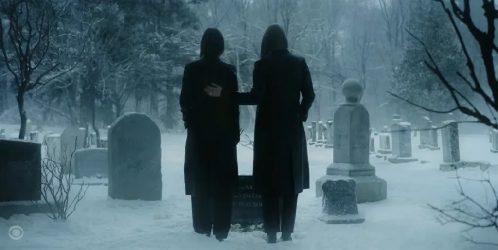 Two women stand in a snowy cemetery.