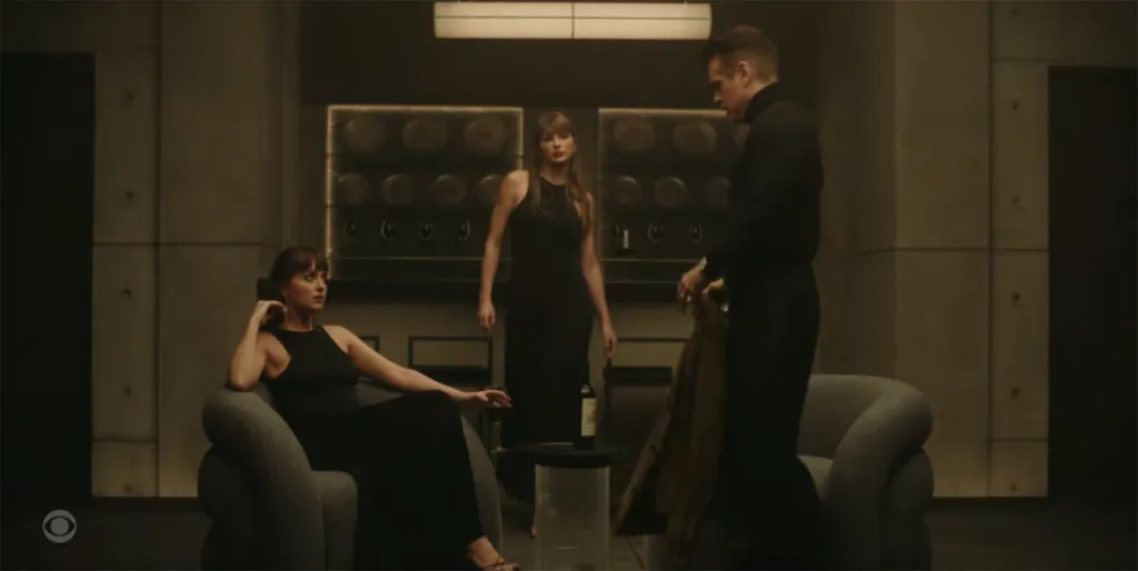Taylor Swift standing in a dimly lit room between a man and a woman, all wearing black.