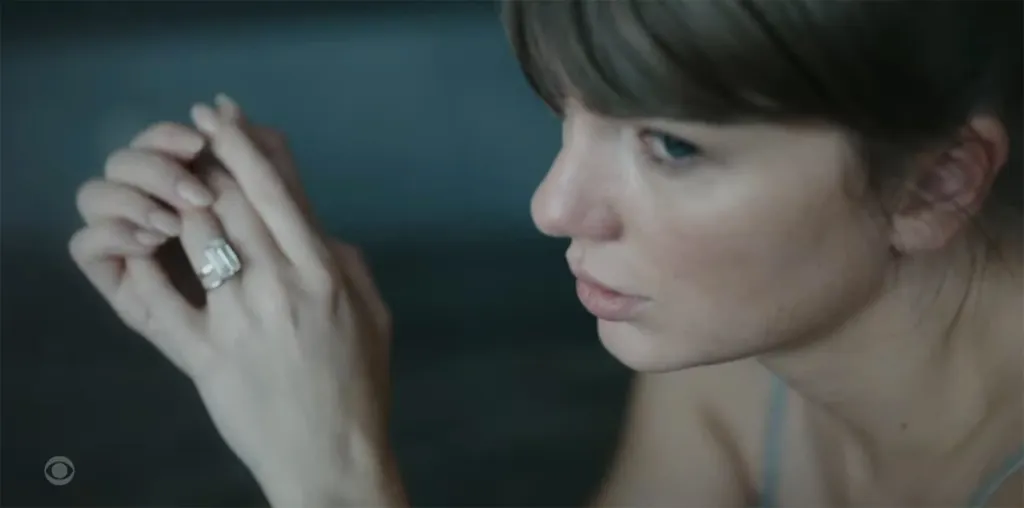 Taylor Swift, in profile, looking down at a large diamond ring on her left hand.