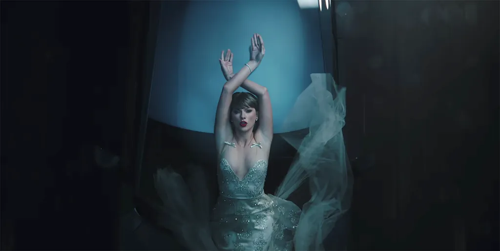 Taylor Swift in a white dress with arms crossed above her head, from her music video