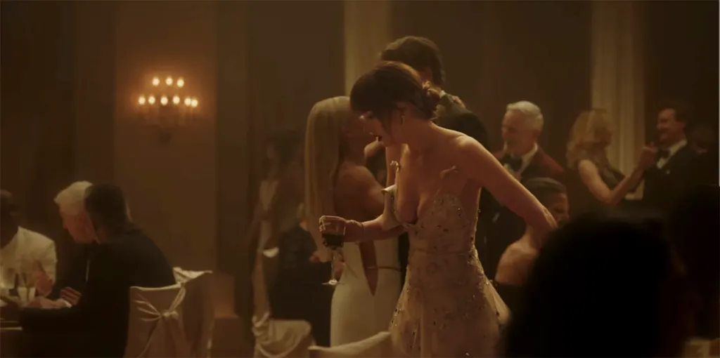 Taylor Swift, in a strapless gown, holding a drink and looking away from the camera in a crowded room.