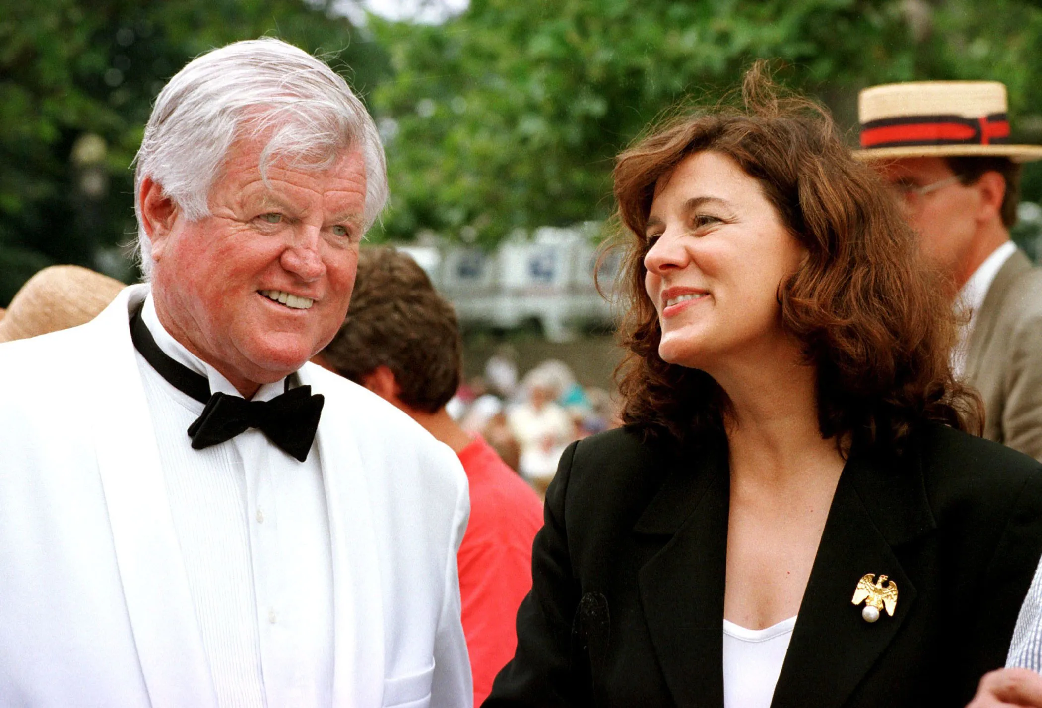 Senator Ted Kennedy in a white tuxedo and black bow tie, smiling at his wife Vicki, who is wearing a black blazer and a gold eagle brooch, smiling back at him.