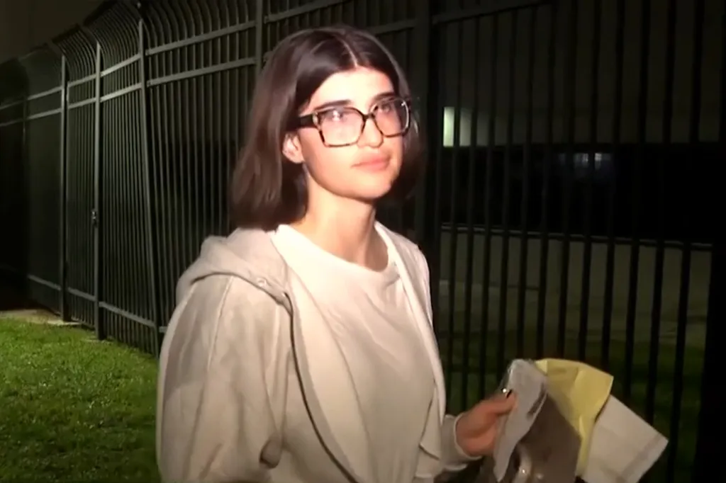 Michelle Luchau-Rebora, 32, wearing glasses, a white t-shirt and light gray jacket, standing in front of black bars.