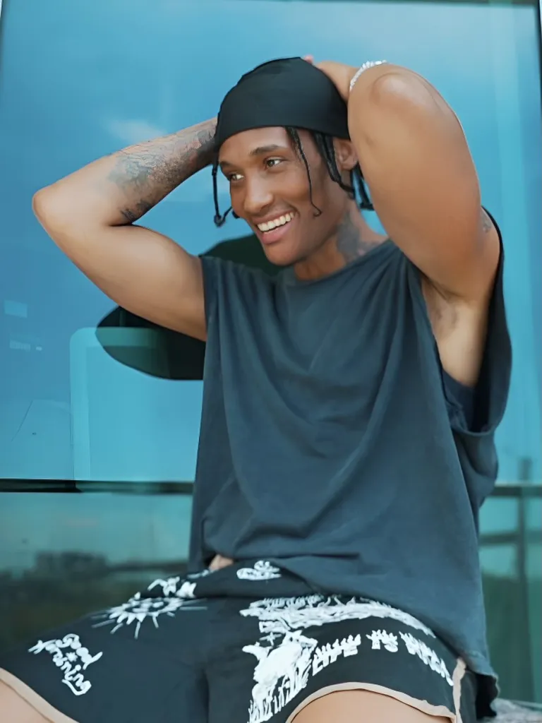 Smiling person wearing a durag and shorts, with their arms raised to their head.