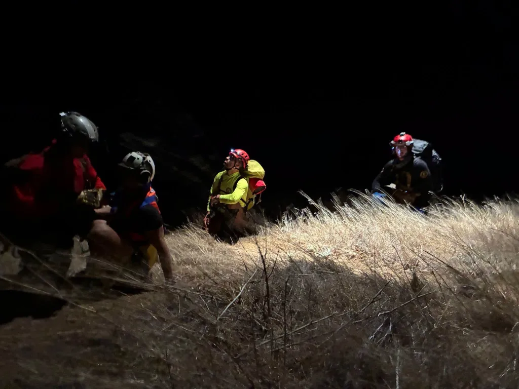 Four search-and-rescue team members with headlamps assisting three hikers at Limekiln State Park in Big Sur at night.