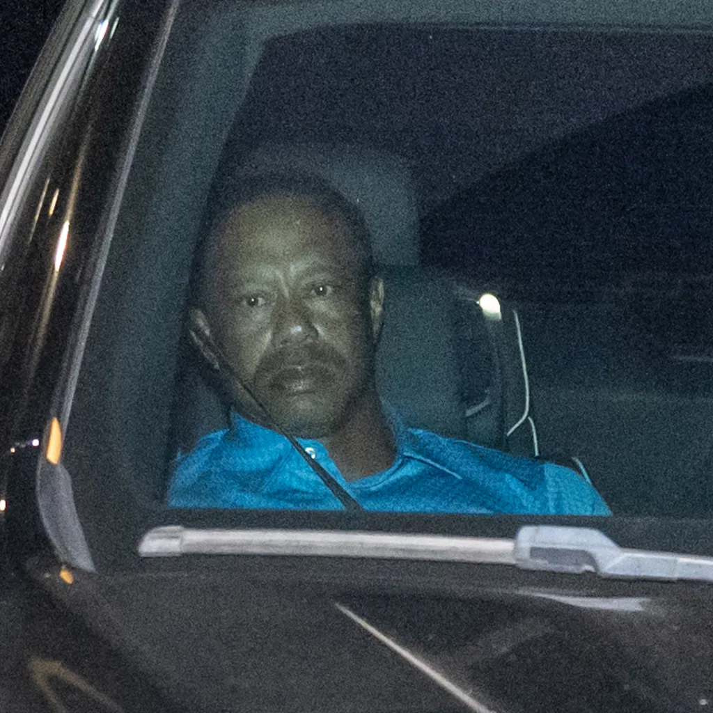 Tiger Woods looks out of a car window, wearing a blue shirt.