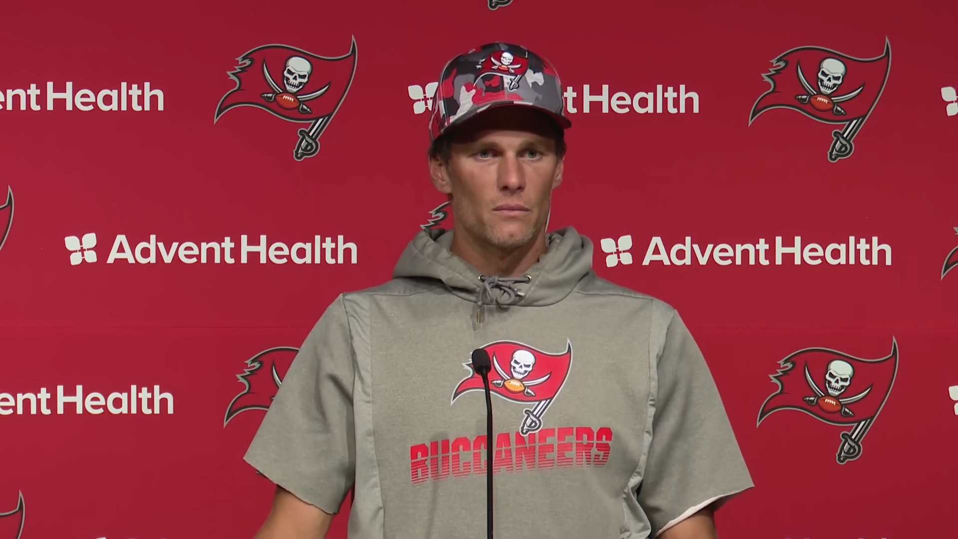 Tom Brady in a camouflage Buccaneers hat and gray Buccaneers hoodie.