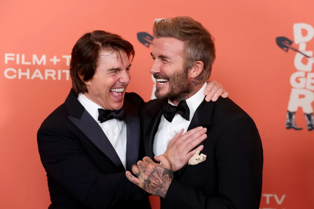 Tom Cruise and David Beckham, both wearing black tuxedos, smiling and laughing together at a film premiere.
