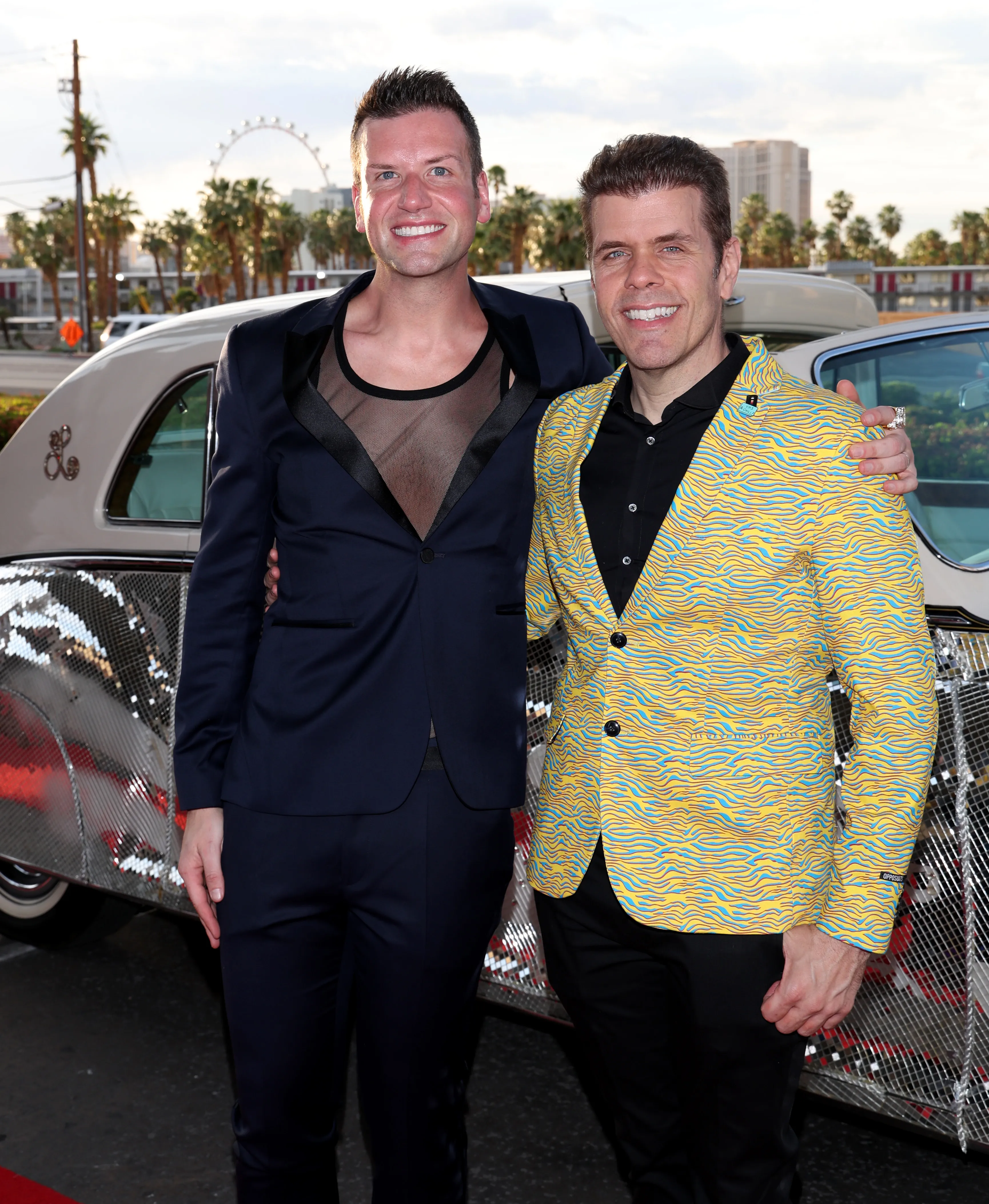 Tom D'Angora (left) and Perez Hilton (right) stand in front of a sequined car.