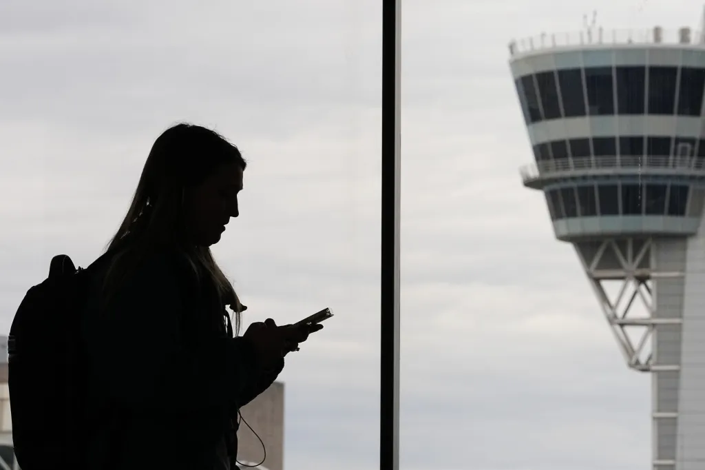 A silhouette of a traveler with a smartphone walks past an air traffic control tower.