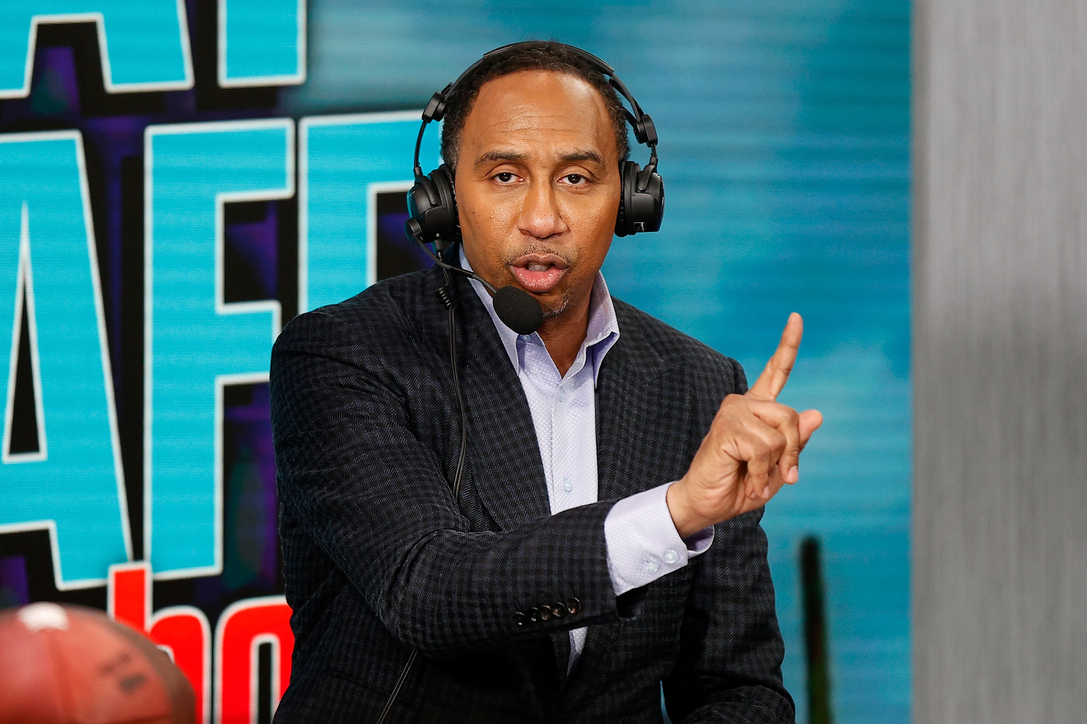 TV personality Stephen A. Smith wearing headphones with a microphone, pointing with his right index finger.