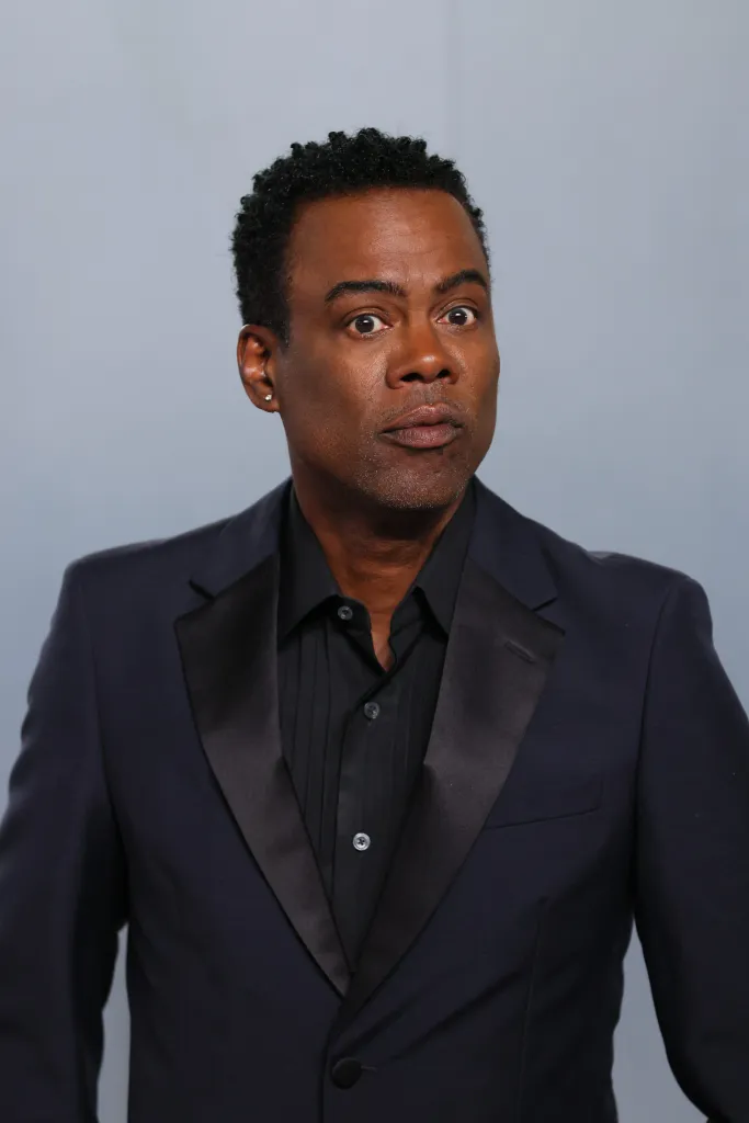 US comedian Chris Rock in a black tuxedo and shirt, with a surprised expression.