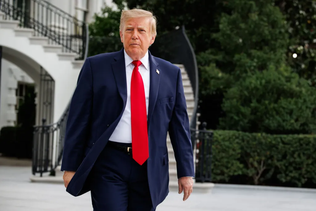 Donald Trump walking out of the White House in a suit and red tie.