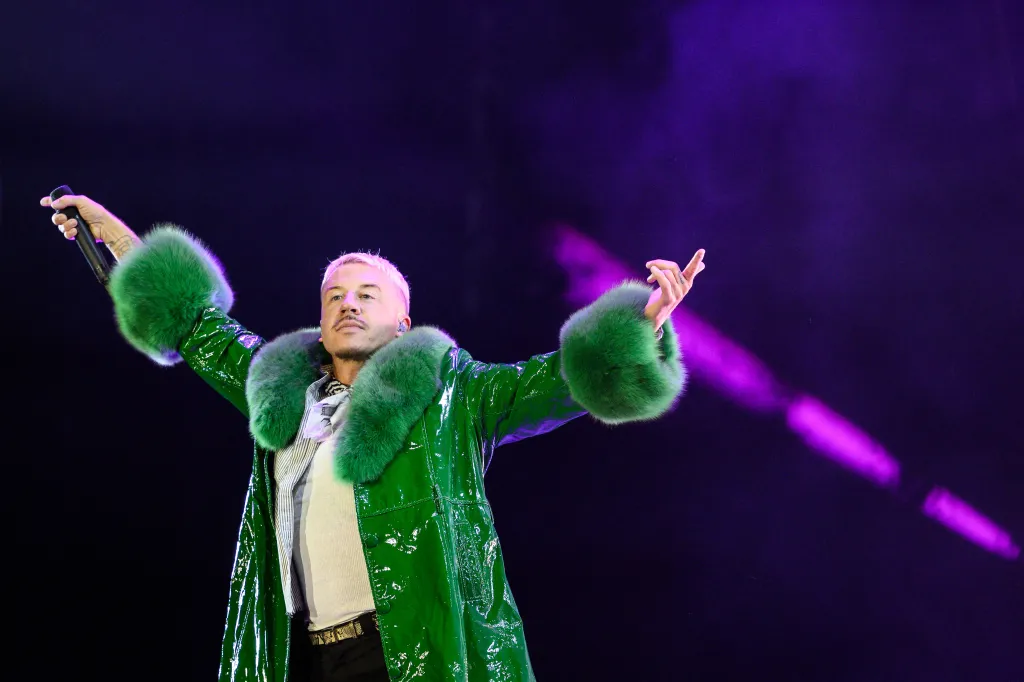 Rapper Macklemore performing on stage in a shiny green coat with fur trim.
