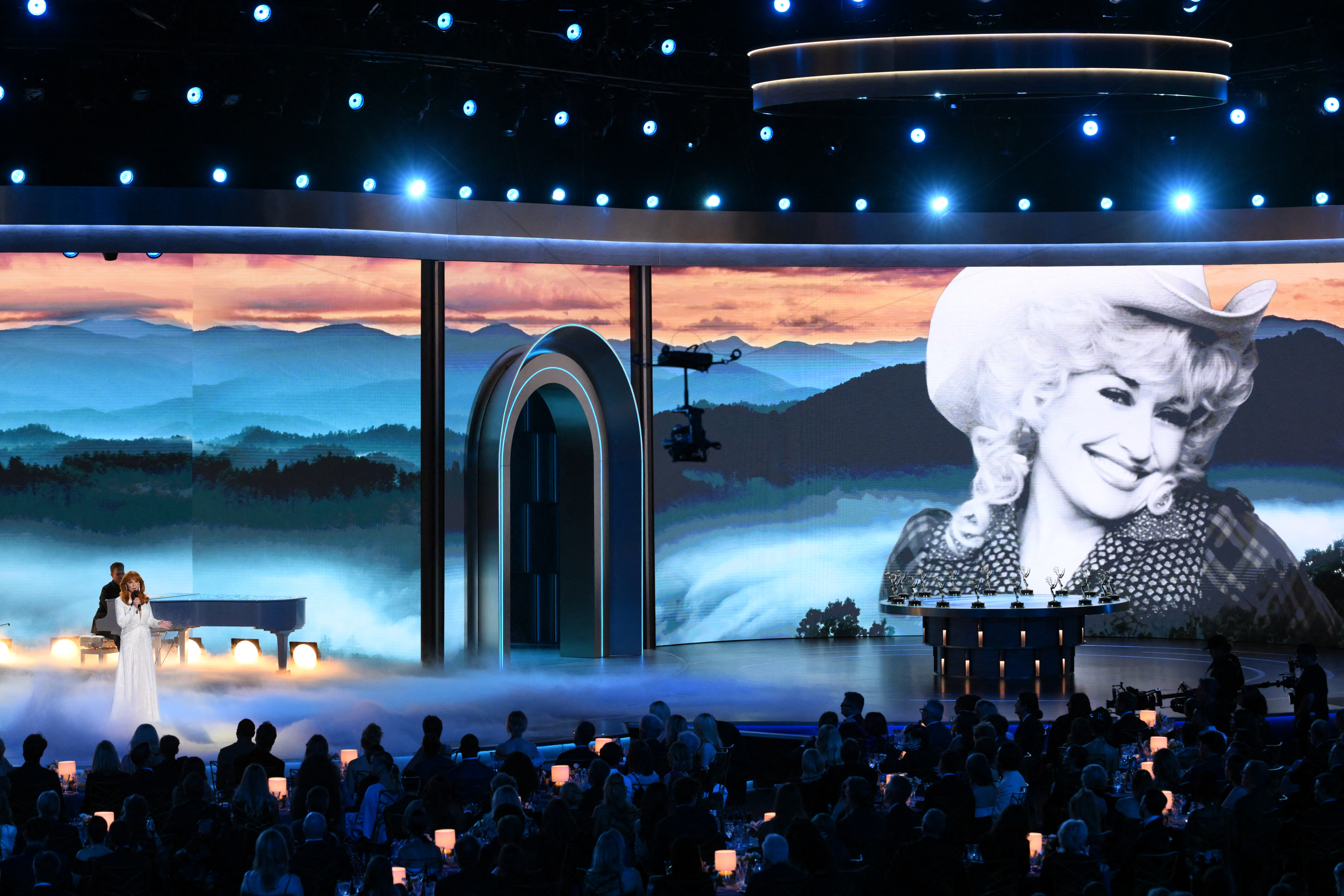 Reba McEntire performing a tribute to Dolly Parton, with images of Parton projected on stage.