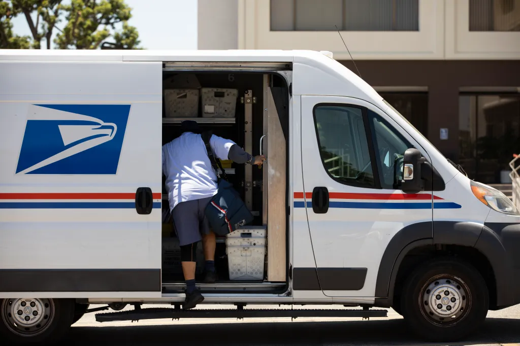 A USPS postal worker delivers mail from a mail truck.