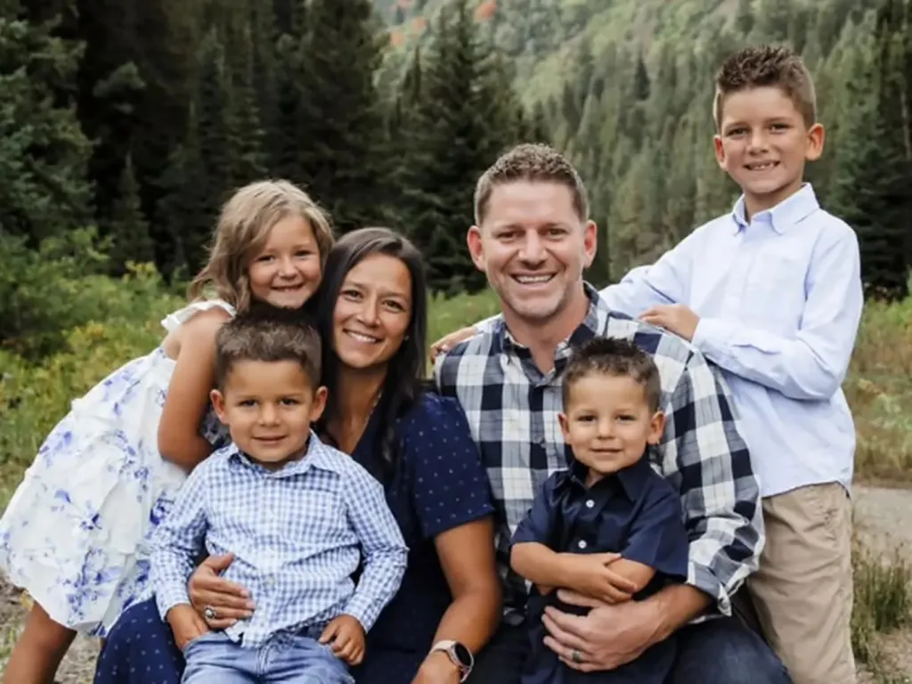 Family portrait of Steve Matheson, his wife, two sons, and daughter smiling in front of a forest.