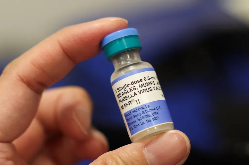 A hand holds a single-dose vial of the Measles, Mumps, and Rubella (MMR) vaccine.