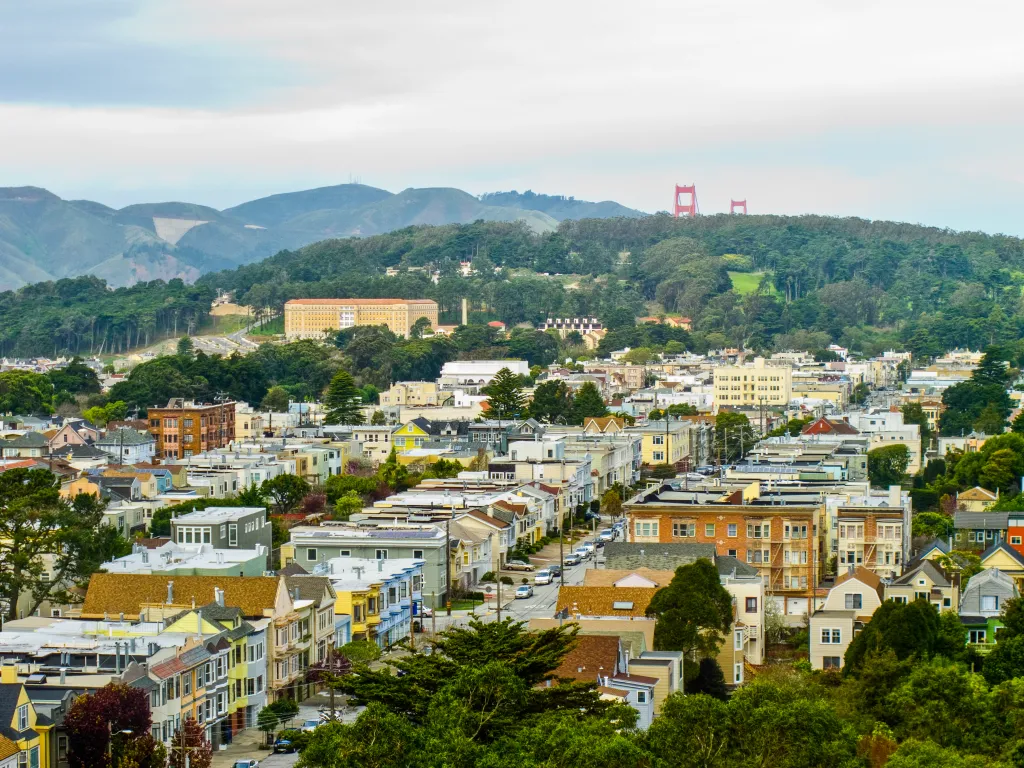 View of the San Francisco cityscape, with residential buildings in the foreground and hills, trees, and the Golden Gate Bridge in the background.