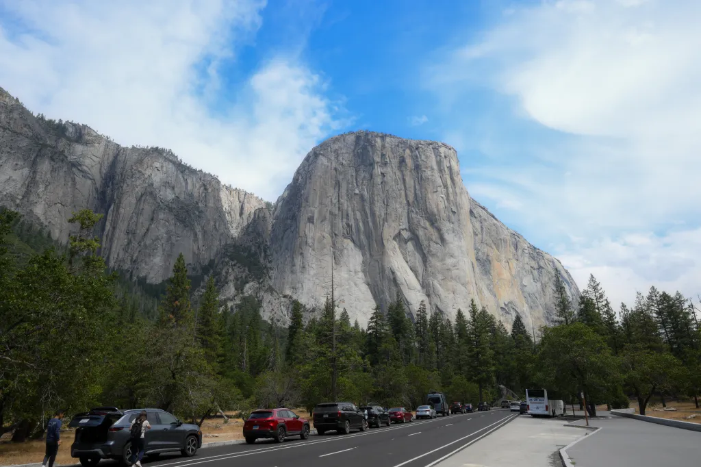 View of El Capitan in Yosemite National Park with tourists and cars parked along a road.