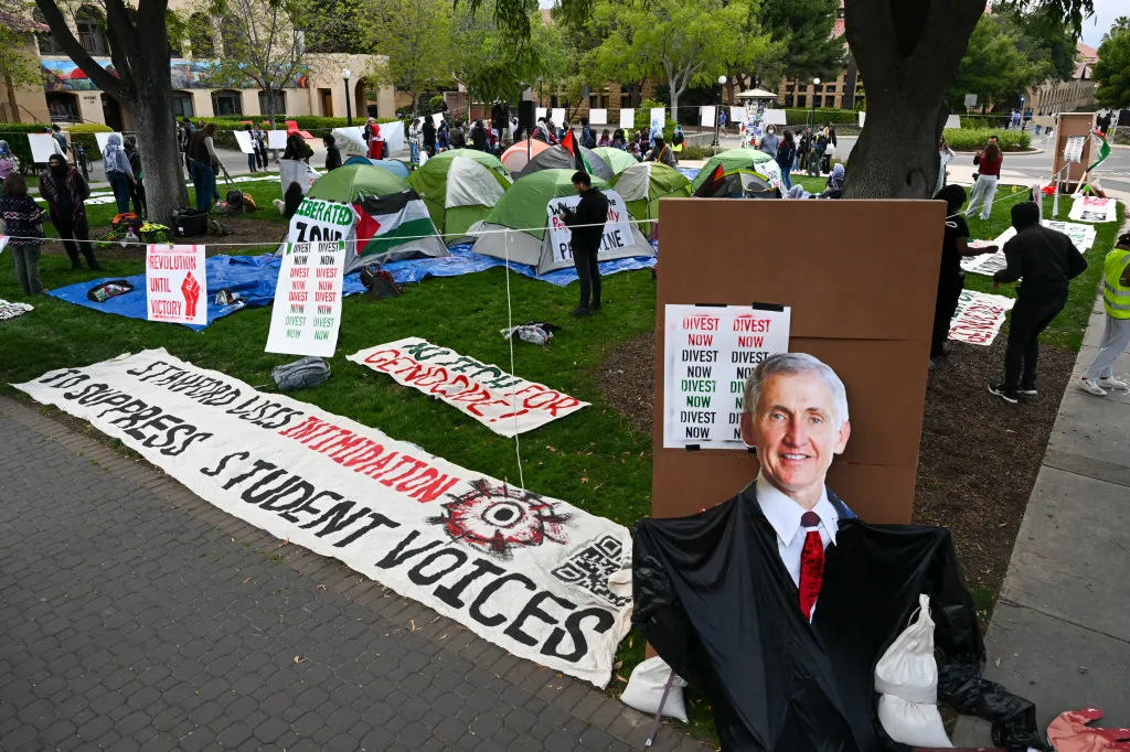 Pro-Palestinian encampment at Stanford University's White Plaza with tents, signs demanding divestment, and a cutout figure of Stanford President Richard Saller.