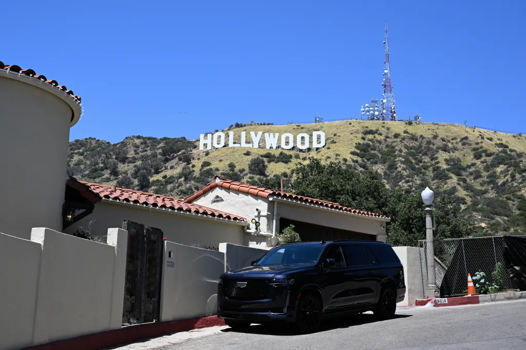 View of the Hollywood Sign on Mount Lee with a black SUV in the foreground.