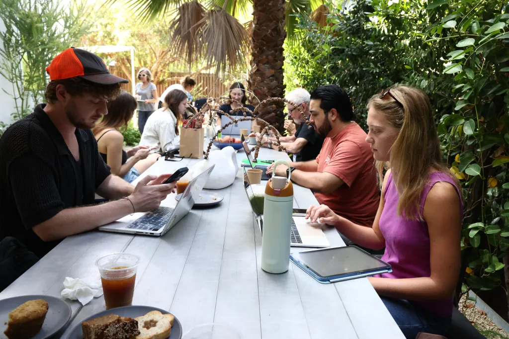 Visitors working on laptops and using phones at an outdoor table at GRANADA, a community gathering space in Los Angeles.