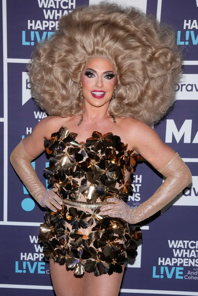 Alyssa Edwards wearing a blonde wig, gold flower-adorned dress, and sheer, sparkly gloves.