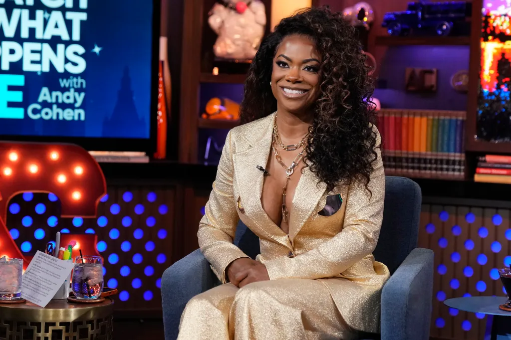 Kandi Burruss smiling while sitting in a chair during an interview.