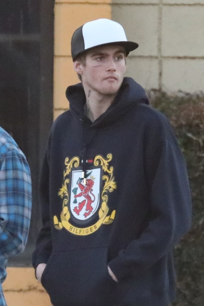 Presley Gerber wearing a black and white hat, a black Tommy Hilfiger hoodie, and a face tattoo.