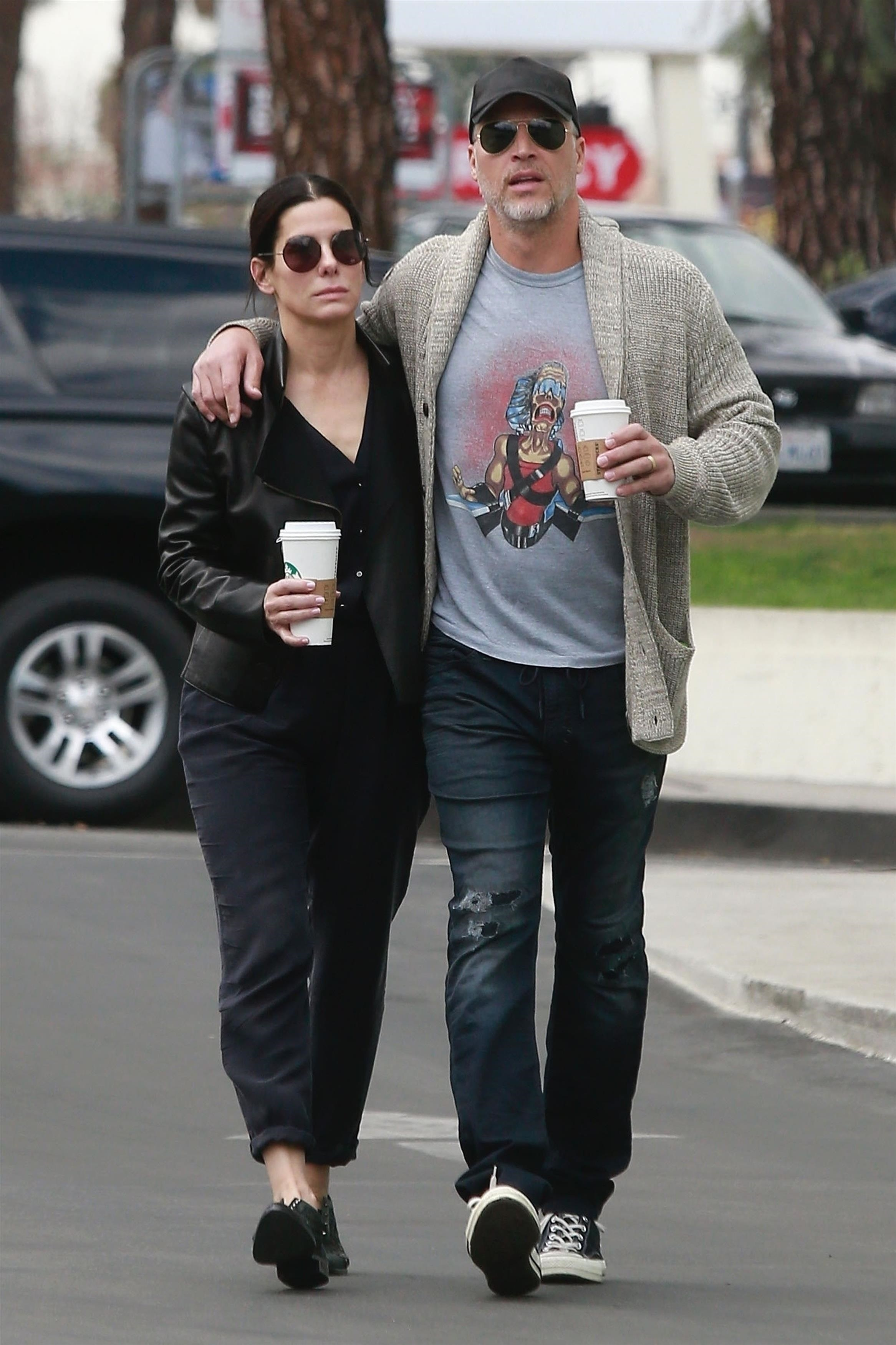 Sandra Bullock and Bryan Randall walk arm-in-arm while holding coffee cups.