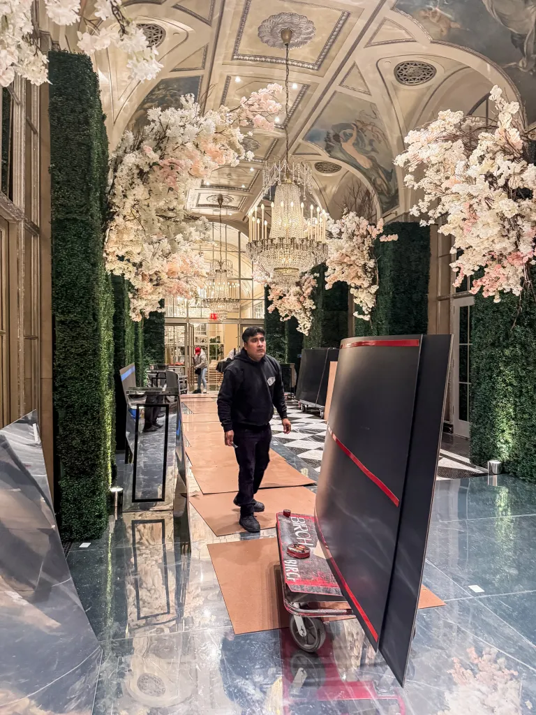 Wedding venue decorated with cherry blossoms, a reflective floor, and hedge walls, with a man walking through it.