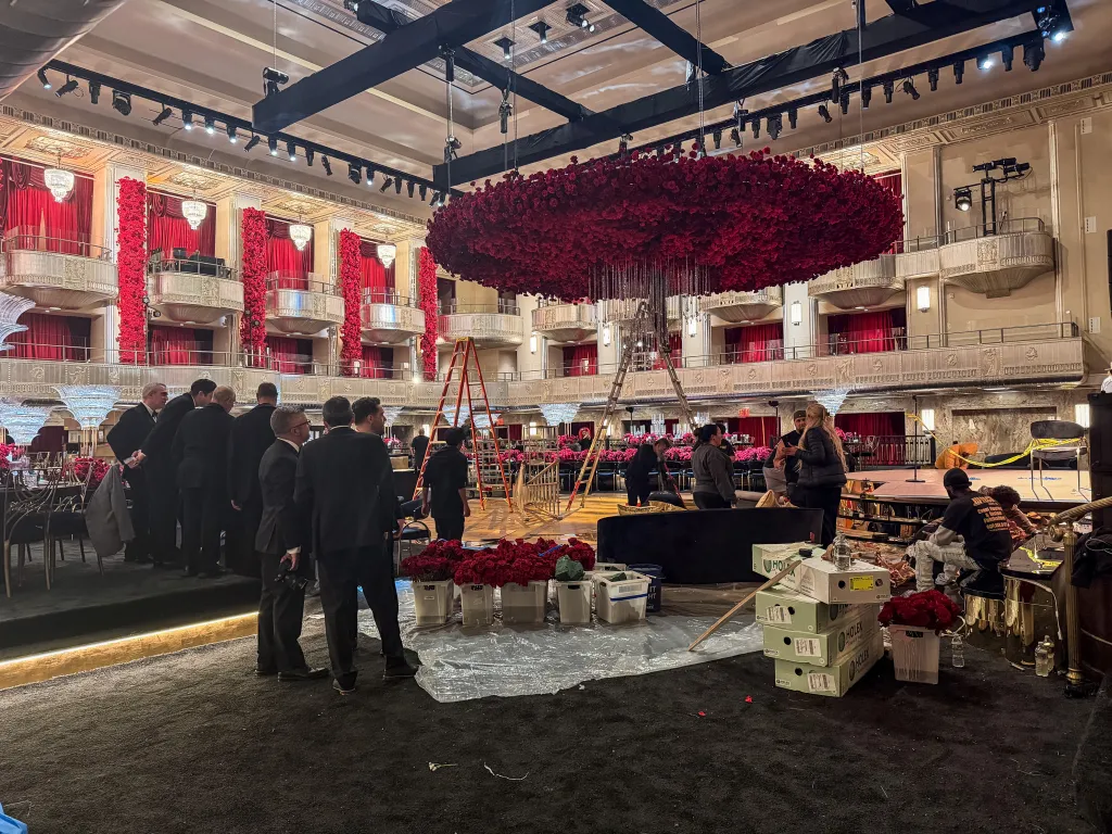 A Waldorf Astoria ballroom is being set up for a wedding, with red roses and cherry blossoms on display.