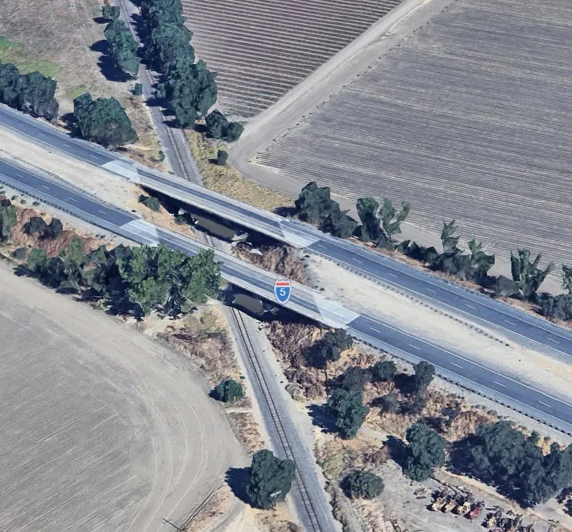 Overhead view of an overpass on Interstate 5 in California, with barren fields and a railroad track nearby.