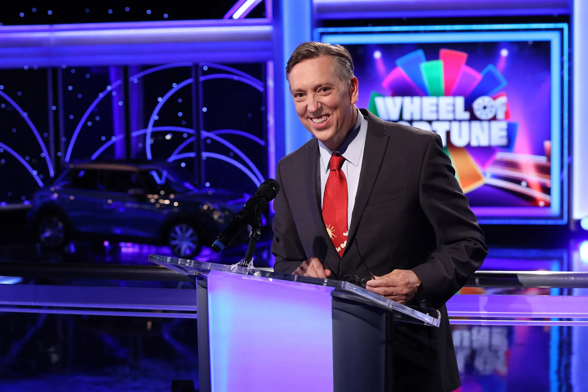 Jim Thornton at a podium in front of the Wheel of Fortune set, with a car in the background.