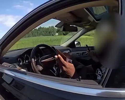 A person inside a car holding a wallet and a phone, viewed from outside the driver's side window.